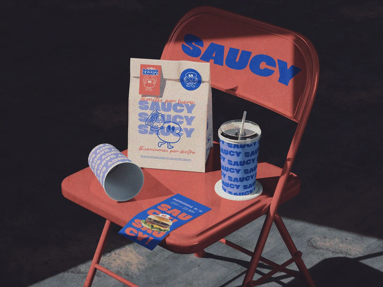 Bolsa, vaso y flyer de Saucy sobre una silla plegable roja con el logo impreso