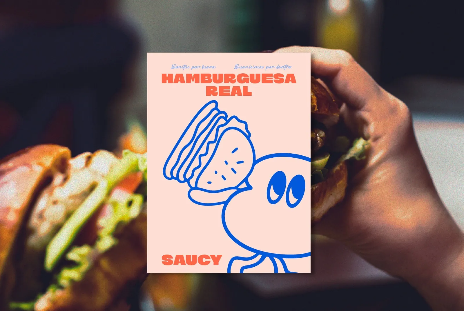 Afiche “Hamburguesa real” de Saucy sostenido frente a una hamburguesa